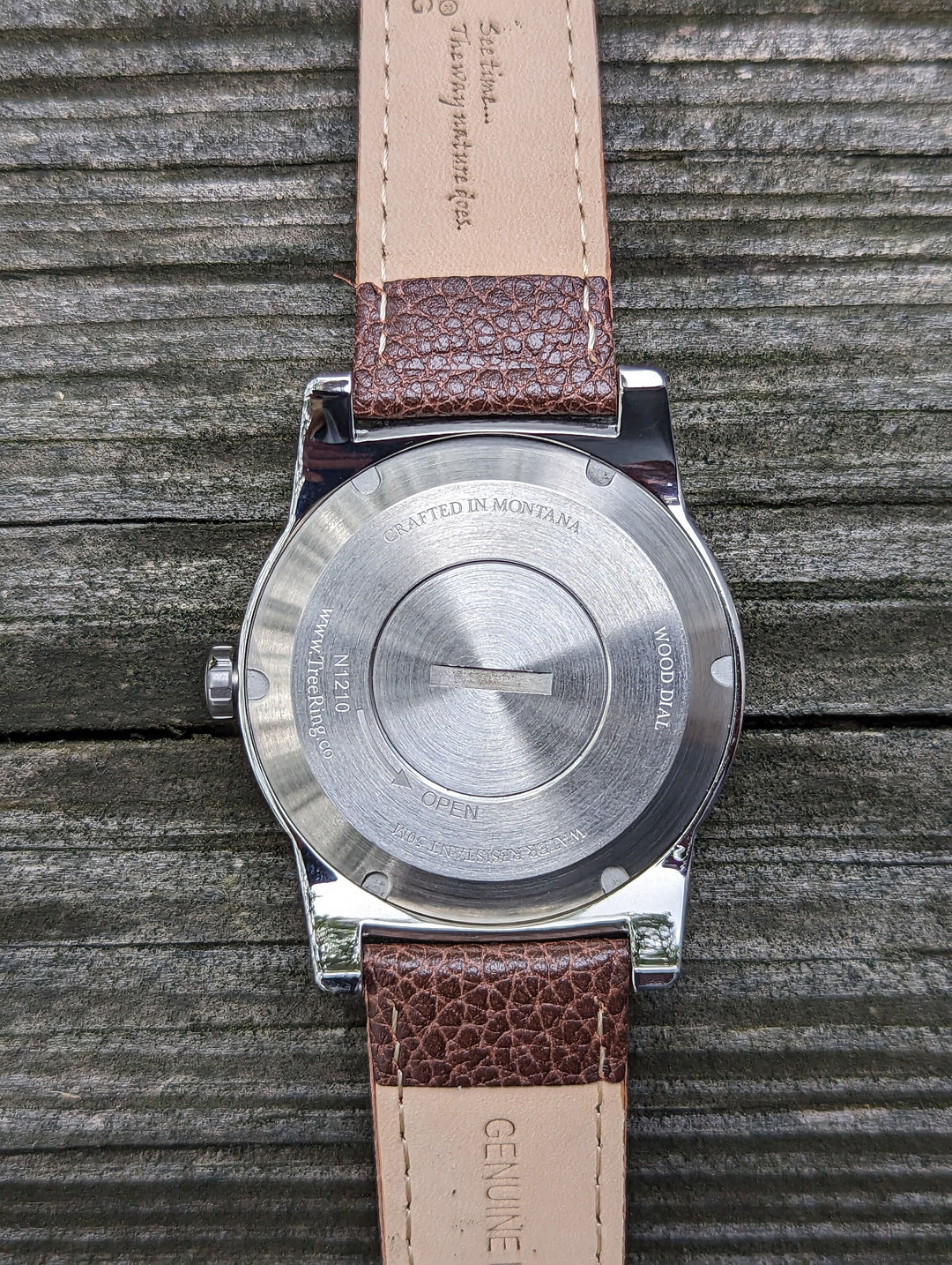 Back view of a watch with engraved details and brown leather strap, highlighting the cremation ashes compartment.