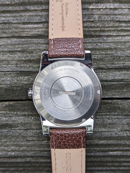 Back view of a watch with engraved details and brown leather strap, highlighting the cremation ashes compartment.