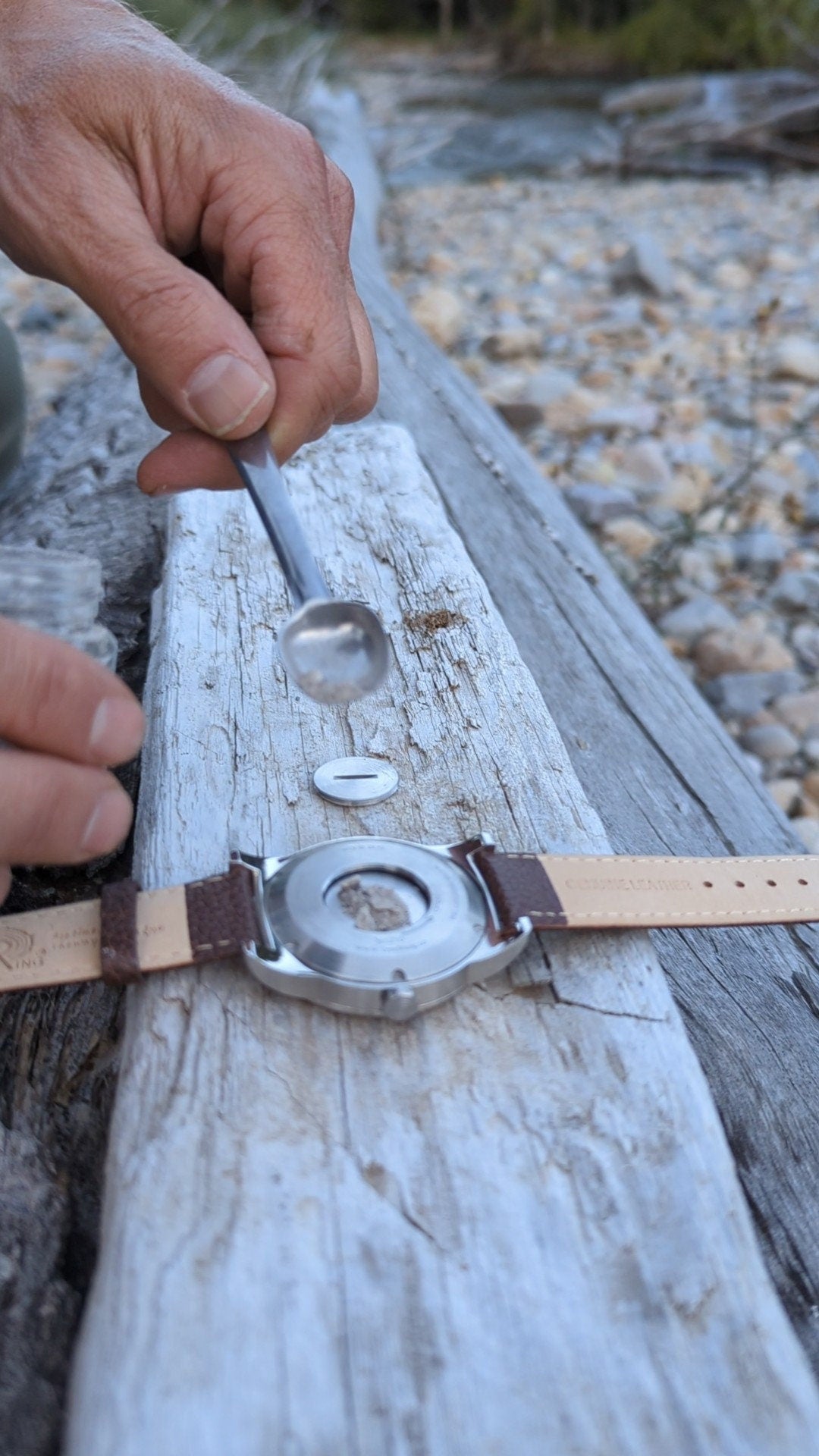 Person using a tool to open the back compartment of a Tree Ring Memorial watch on a wooden surface.