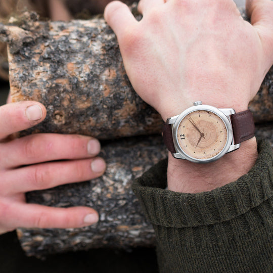 Person holding logs wearing a Classic Wood Watch, showcasing tree rings representing years of nature's history.